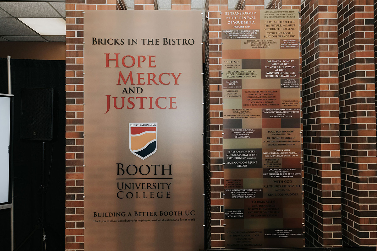 Two large plaques on a brick wall. One reads Bricks in the Bistro: Hope, Mercy and Justice with the Booth UC logo. The other shows donor names in a brick pattern.