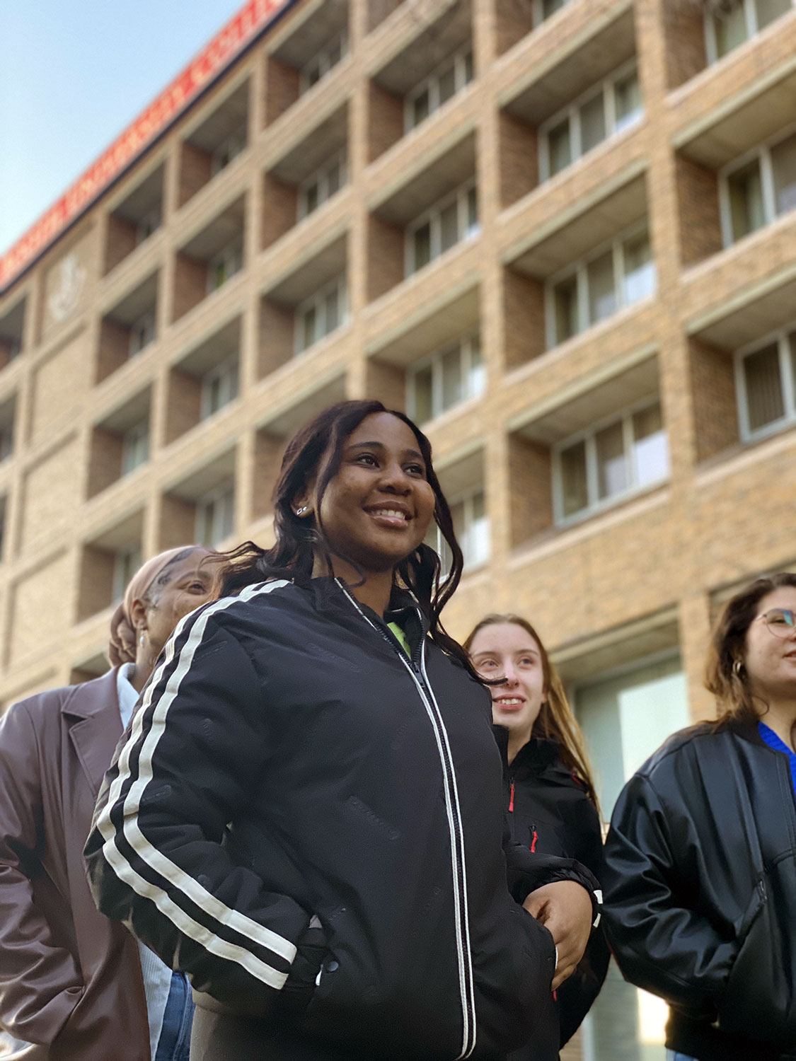 An international student standing with friends outside the main campus building.