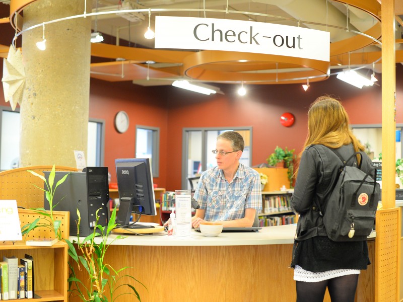 A student at a library check-out desk talking to a librarian