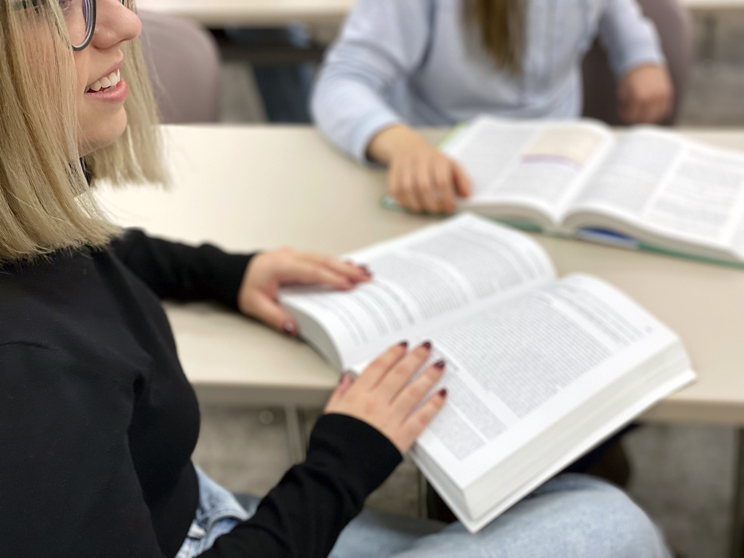 A woman holding a textbook open on her desk.