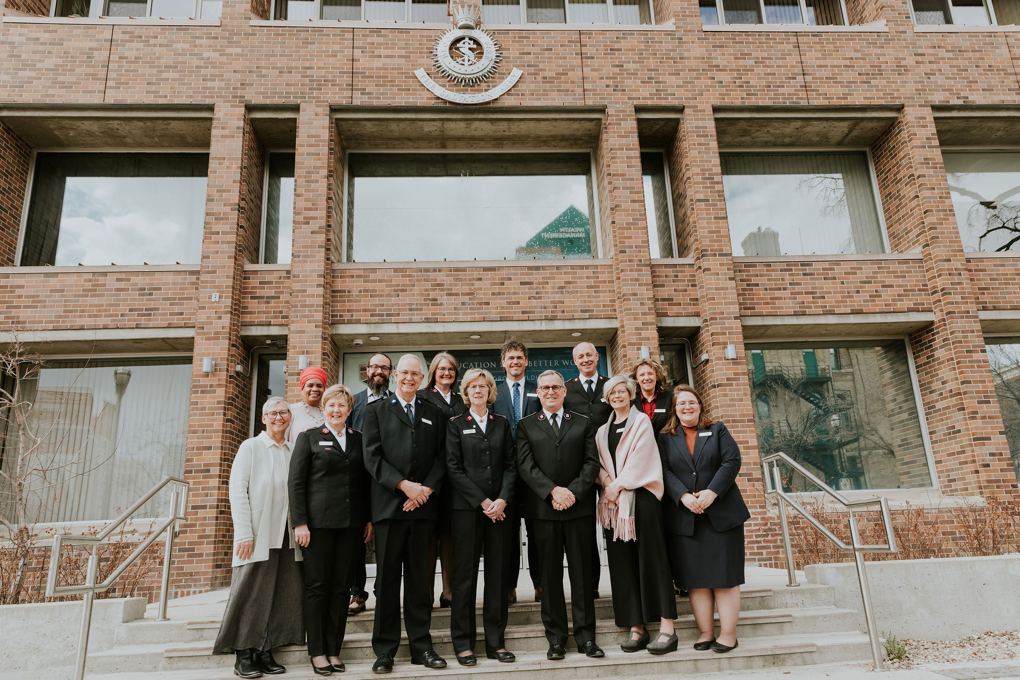 A group of staff and administrators stand for a photo in front of a brick building.