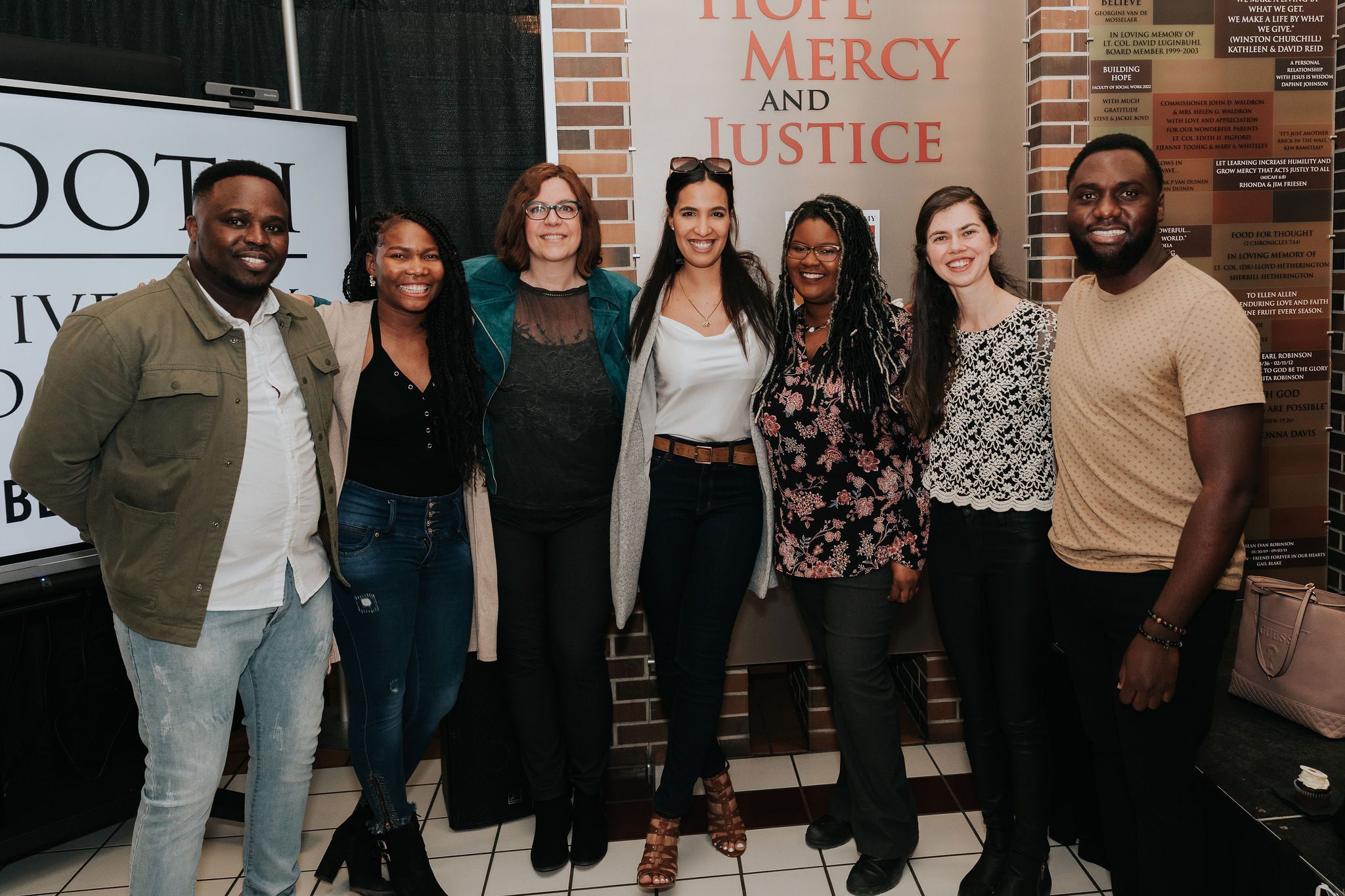 A group of seven alumni and staff standing together, smiling at the camera.