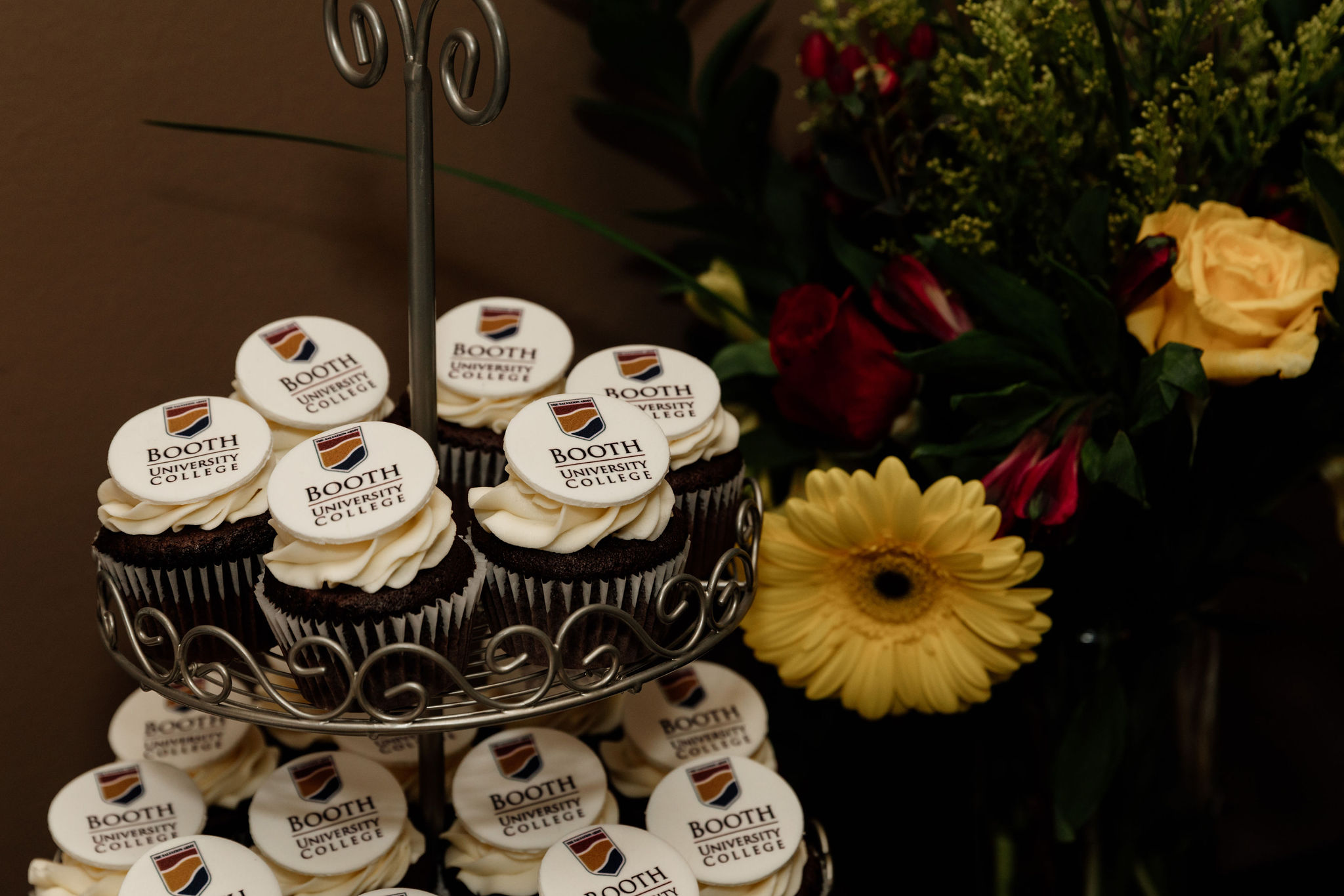 Cupcakes with white icing and the Booth UC logo displayed on a tiered rack.