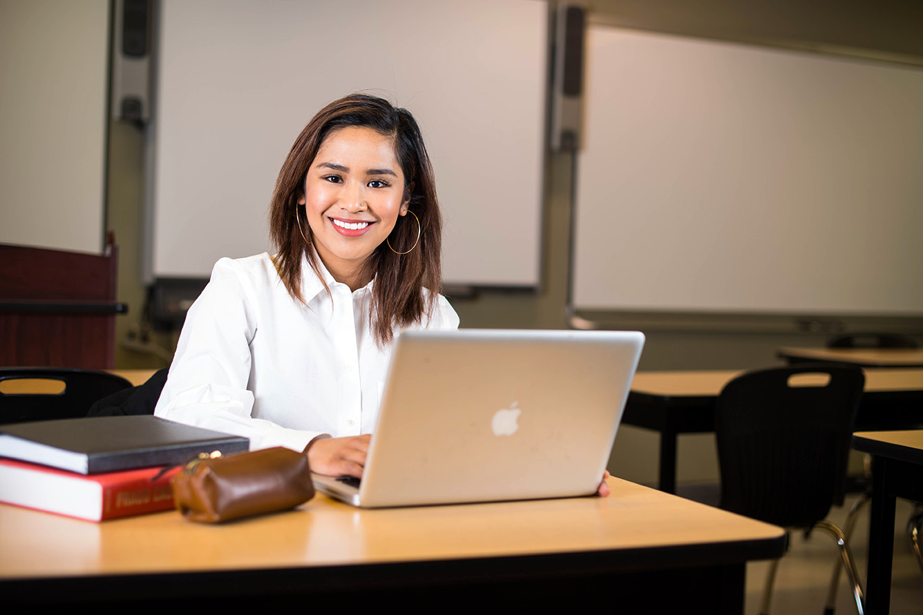 A woman typing on her laptop computer and smiling at the camera.