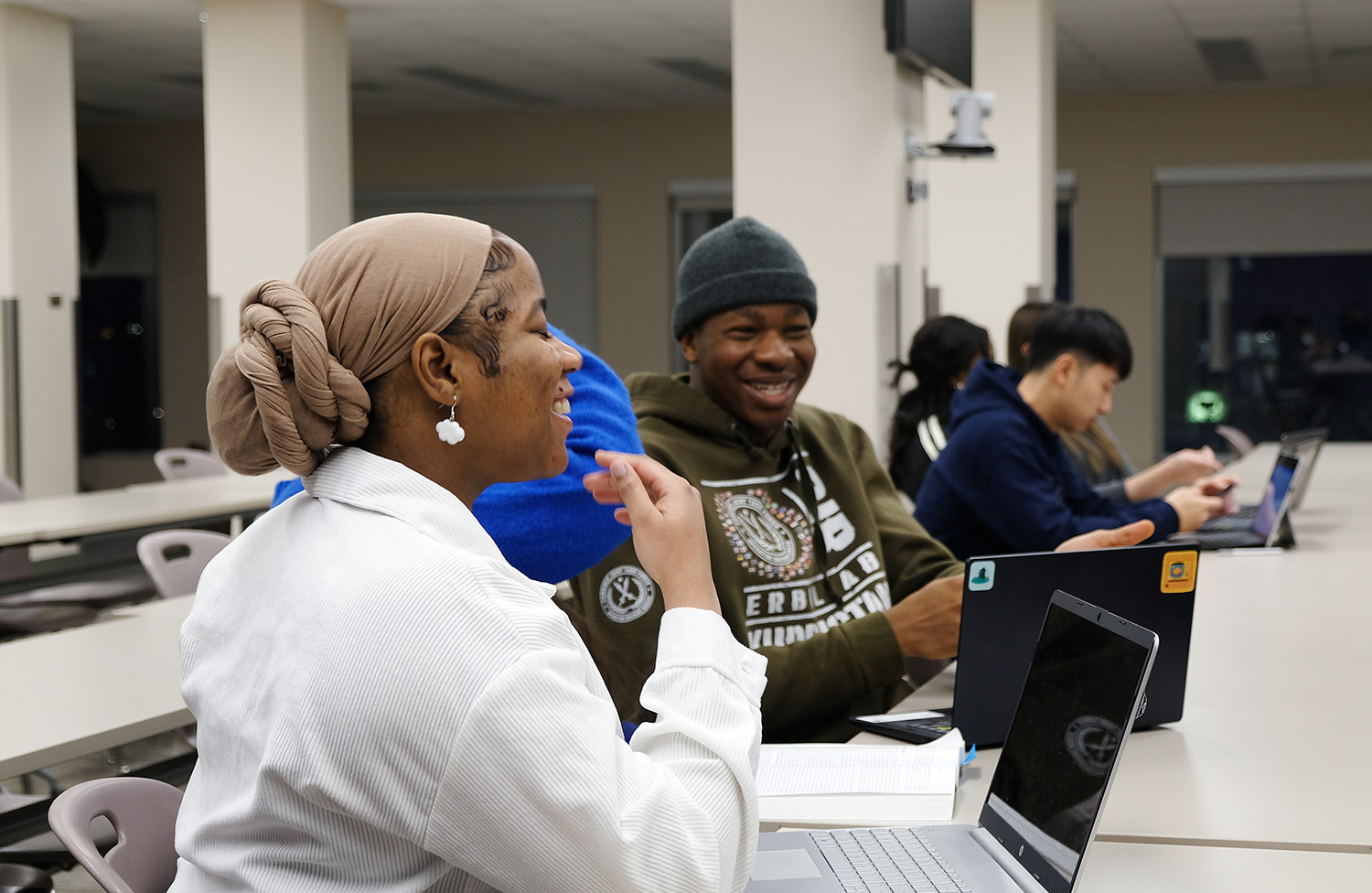 Students sitting at a desk with their laptop computers, laughing together.