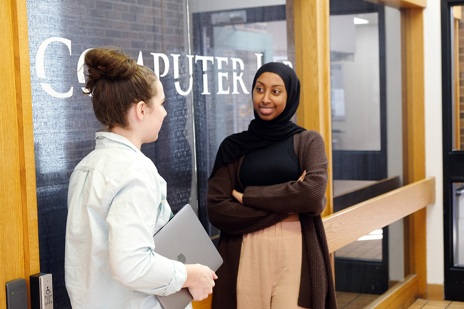 Two students standing outside the computer lab chatting.