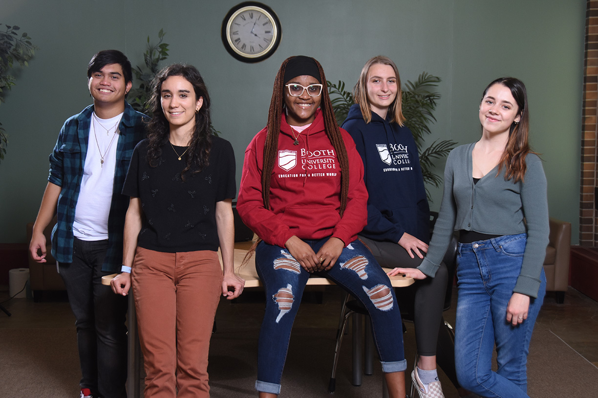 A group of five students sitting or leaning on a table, smiling at the camera.