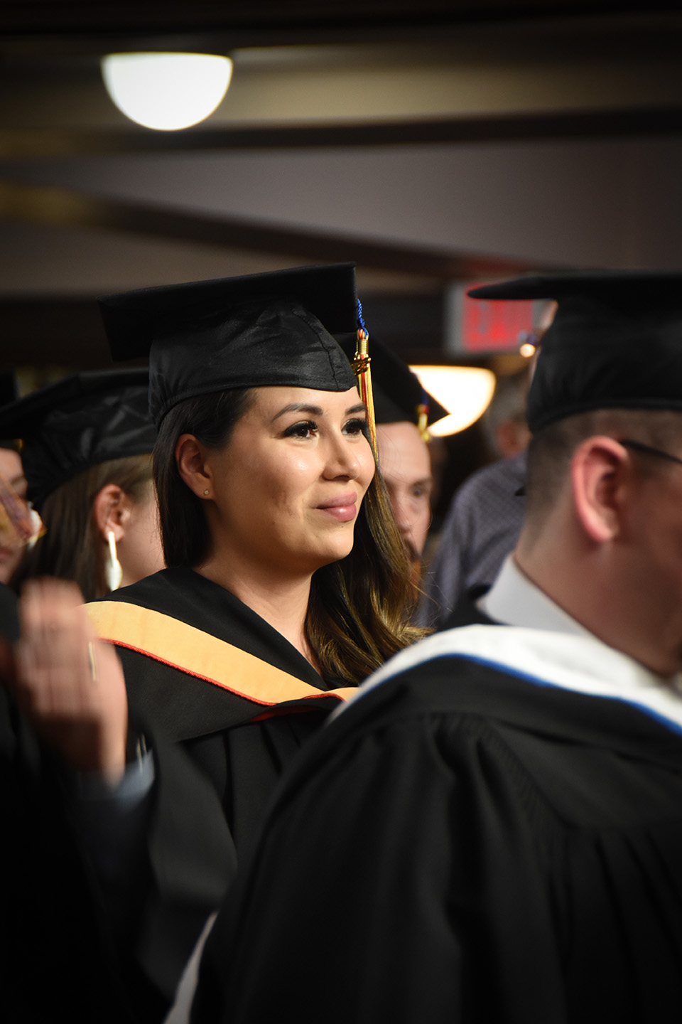 A woman in her graduation gown and cap, surrounded by other graduates.