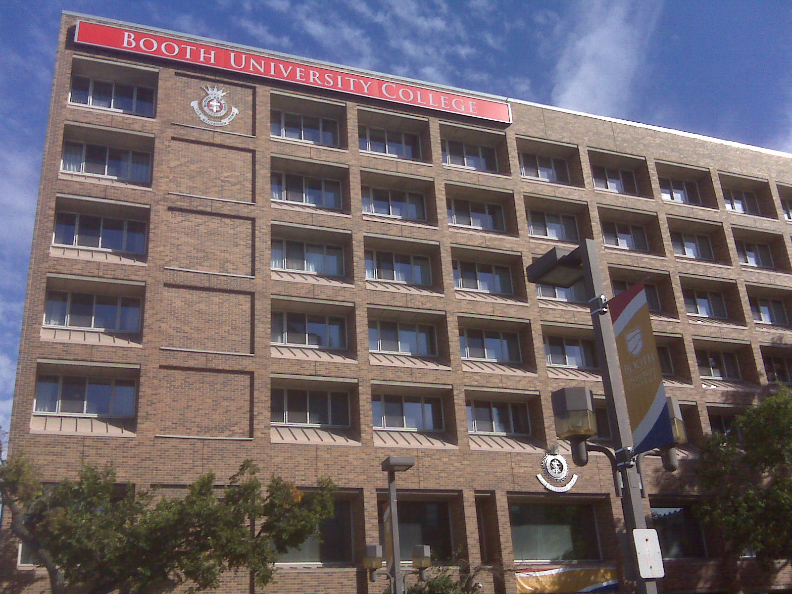A seven-story brick building with a red sign across the top reading Booth University College.