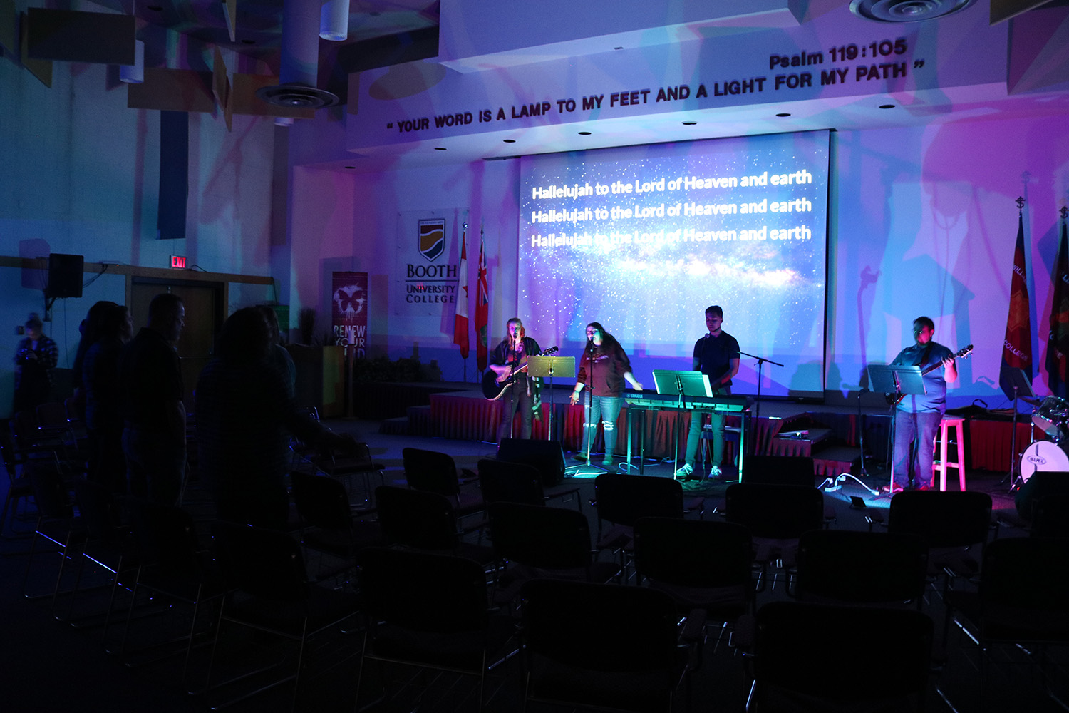 Four students sing at microphones with lights dimmed and a projector shining lyrics behind them.