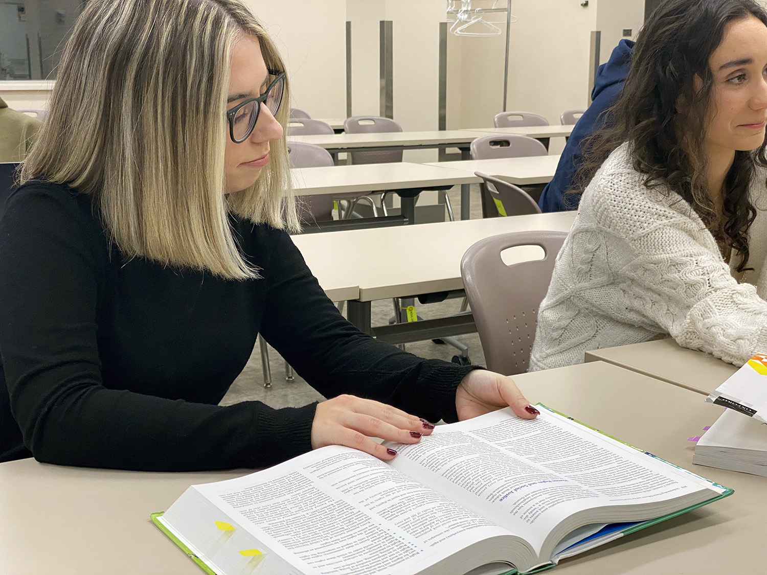 A female student sits at a desk reading a textbook.