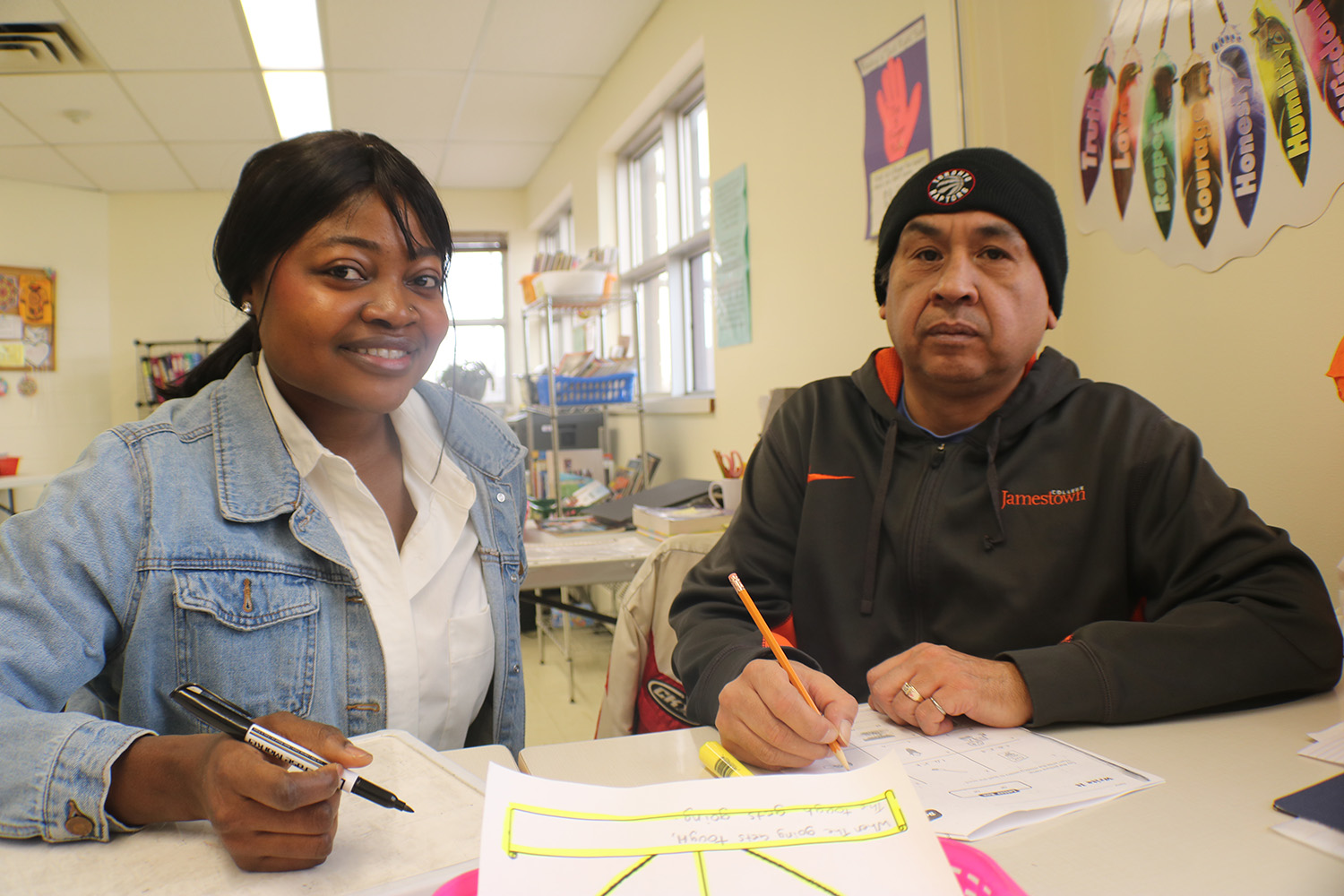 A female students sits next to a man at a table with papers.