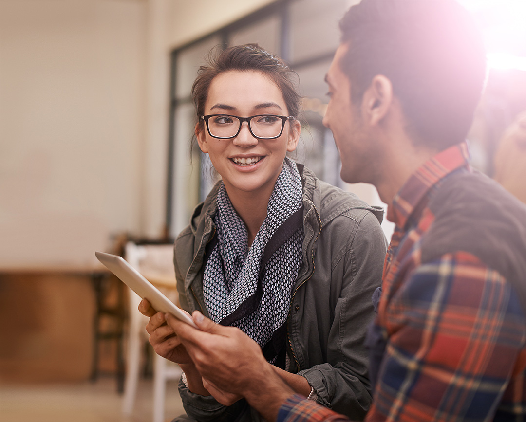 Two students looking at each other and smiling, one is holding a tablet.