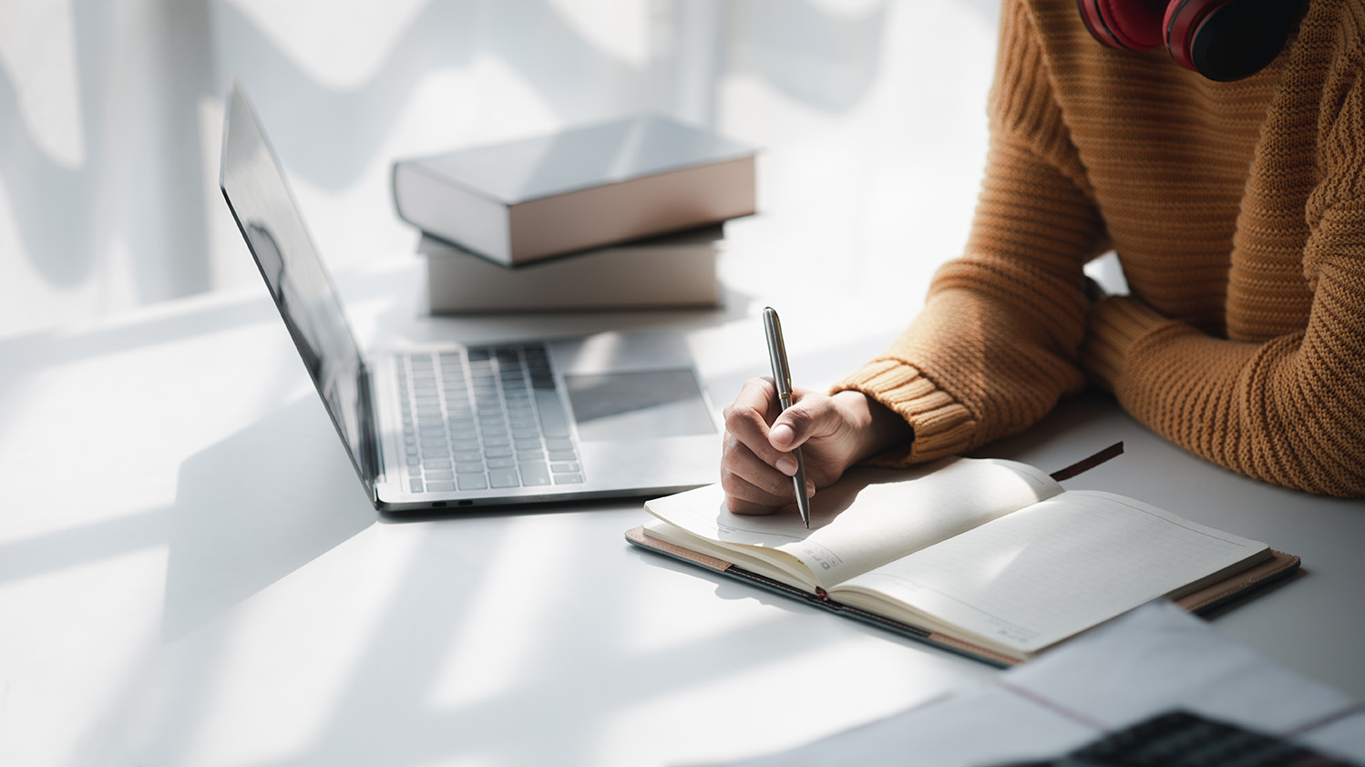 Woman sitting next to computer, writing in notebook.