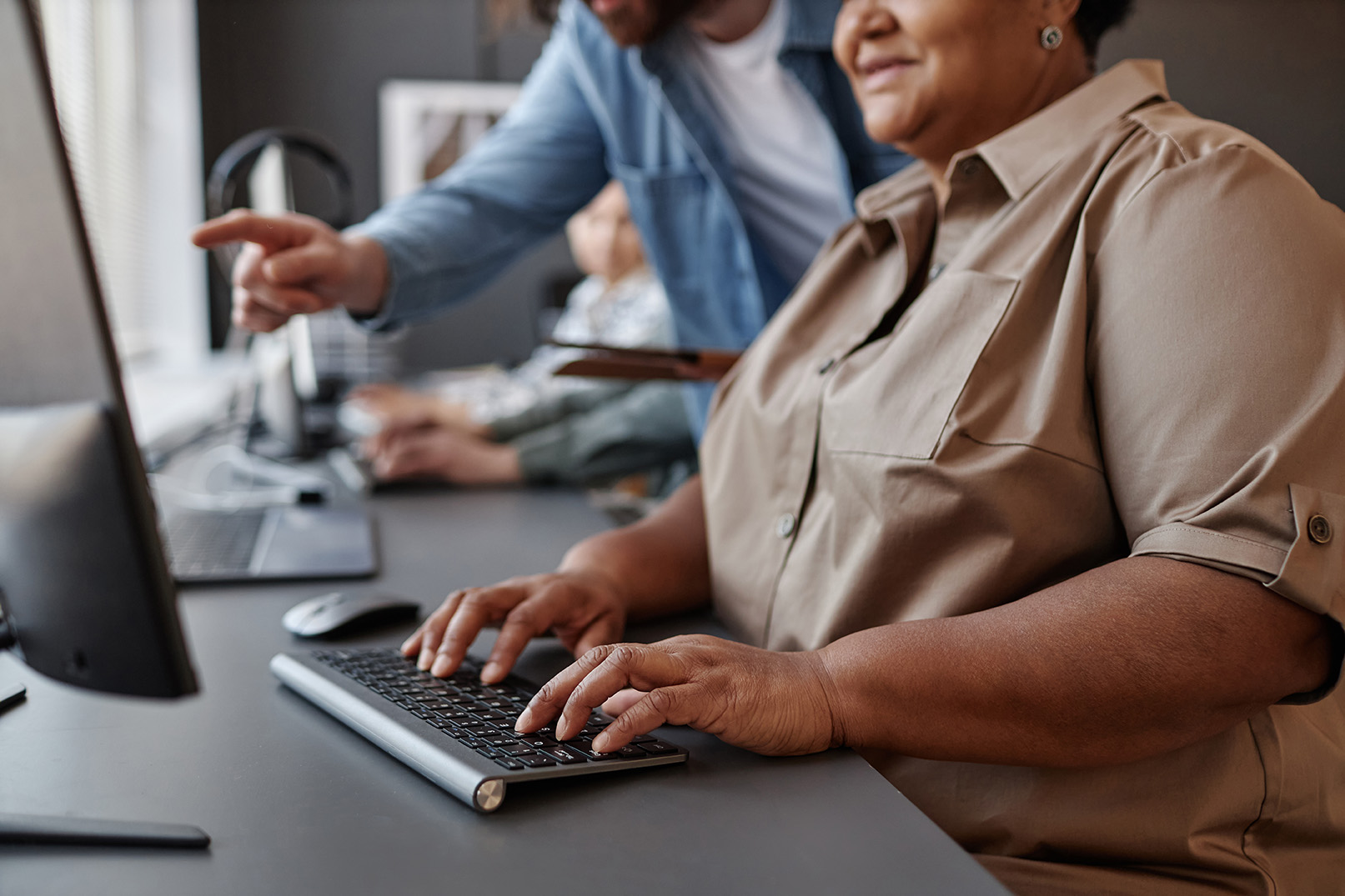 Woman typing on a keyboard with instructor looking over her shoulder.