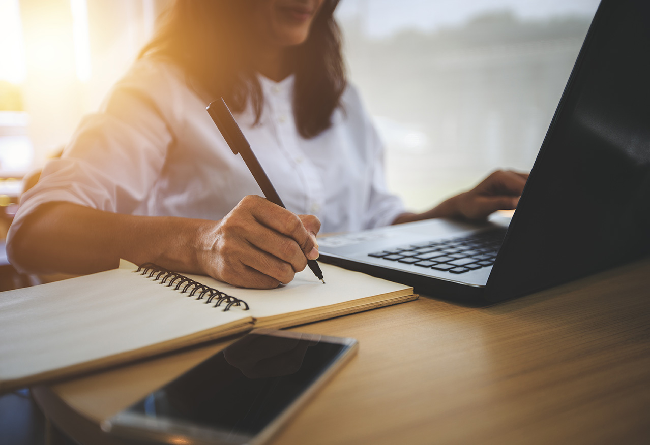 Woman at a computer taking notes.