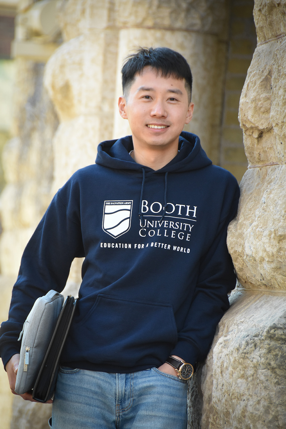 Josh leaning against a wall, holding a binder at his hip.