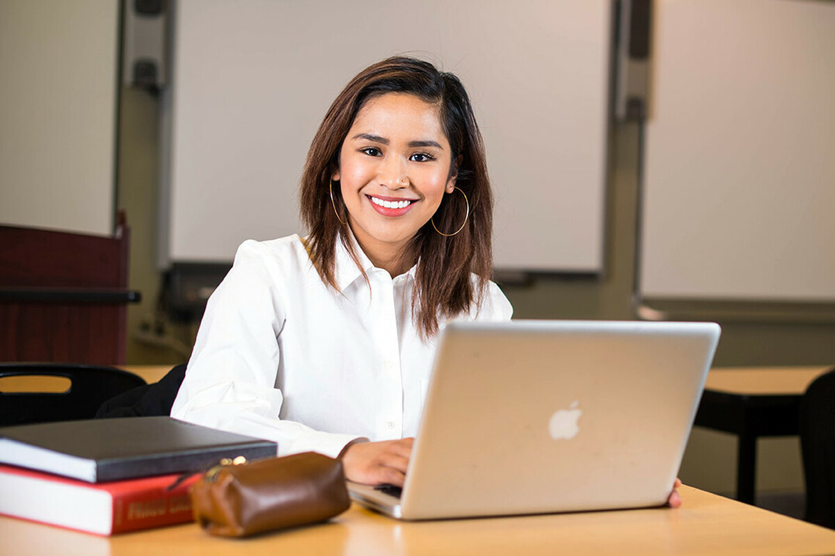 A woman typing on her laptop computer and smiling at the camera.