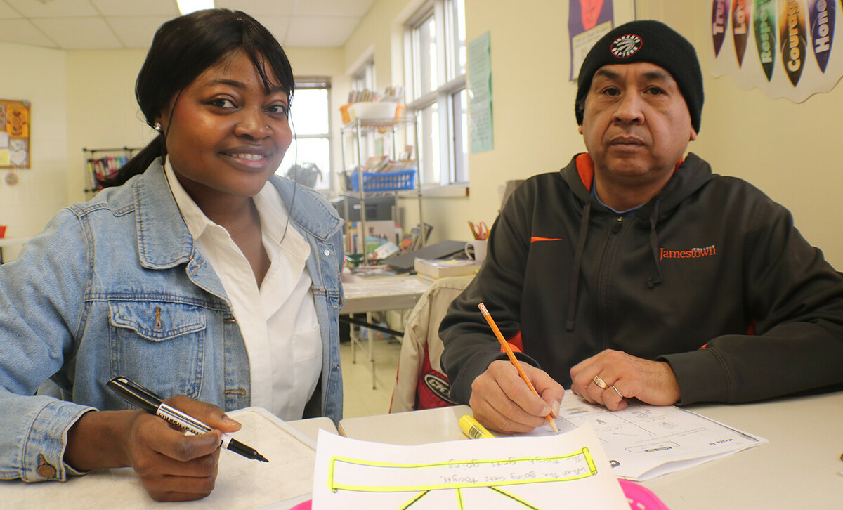 A female students sits next to a man at a table with papers.